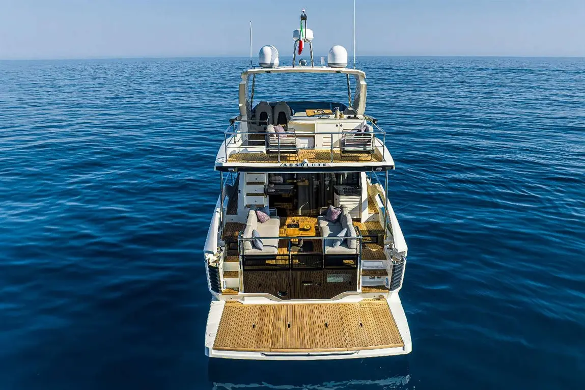 Luxury yacht "Absolute" anchored on calm blue waters, featuring stylish outdoor seating and a wooden deck area.